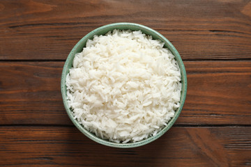 Bowl of tasty cooked rice on wooden background, top view