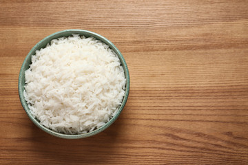 Bowl of tasty cooked rice on wooden background, top view. Space for text