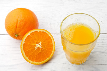 One whole and half of orange next to a glass of fresh orange juice isolated on white painted wood.