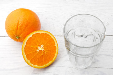 One whole and cut half of orange next to an empty glass isolated on white painted wood.