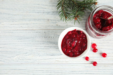 Bowl and jar with tasty cranberry sauce on white wooden background, flat lay. Space for text