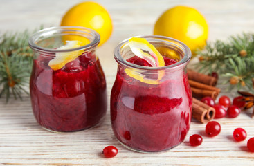 Tasty cranberry sauce with citrus zest in glass jars on table