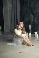 Little blonde girl in white dress in room with candles 