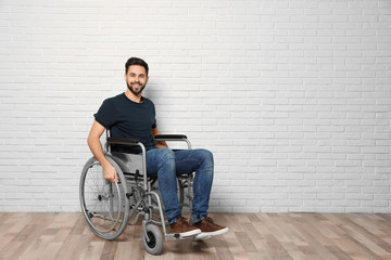 Fototapeta na wymiar Young man in wheelchair near brick wall indoors. Space for text