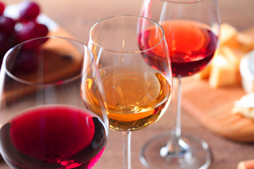 Glasses with different wines and appetizers on wooden table, closeup
