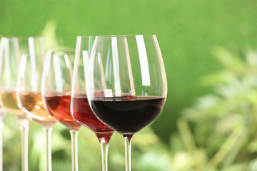 Row of glasses with different wines against blurred background, closeup. Space for text