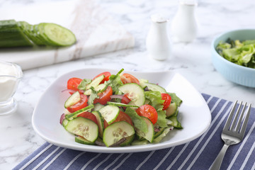 Plate of vegetarian salad with cucumber, tomato, lettuce and onion served on table