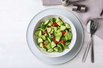 Bowl of vegetarian salad with cucumber, tomato and lettuce served on table, flat lay