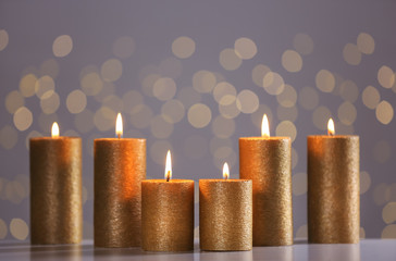 Burning gold candles on table against blurred lights. Space for text