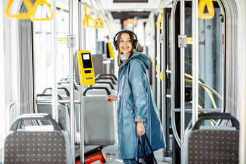 Young stylish woman with headphones while moving in the modern tram. Happy passenger enjoying trip at the public transport