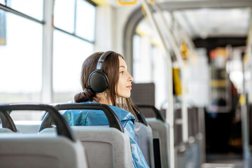 Young woman passenger enjoying trip at the public transport, sitting with headphones in the modern...
