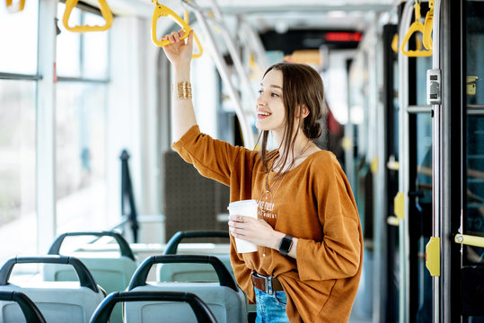 Young and happy passenger enjoying trip at the public transport, standing with coffee in the modern tram