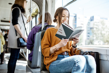 Young woman reading book while moving in the modern tram, happy passenger at the public transport