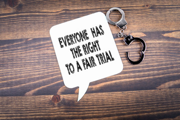 Everyone has the right to a fair trial. Handcuffs and speech bubble on a dark wood background