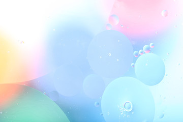 Drops of oil in water on a colored background. Abstract background with light blue, pink, yellow and green circles of different sizes. Blurred, horizontal, place for text. Design concept.