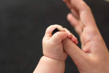 Kid's hand holds the finger of his mom's hand on a black background