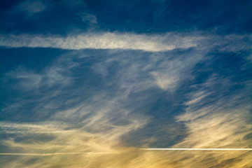 Clouds with jet trails from planes in the sunset sky with yellow reflections. Suitable for use as a background or cover for a book, report, presentations, slides, brochures, flyers.