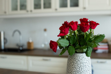 Vase with red roses in white kitchen interior