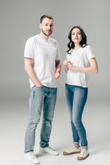 young man and woman in white t-shirts and blue jeans looking at camera on grey background