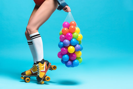 Cropped View Of Woman In Knee Socks And Roller Skates Holding String Bag With Colorful Balls On Blue