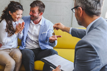 Real estate agent handing over house keys to young married couple 