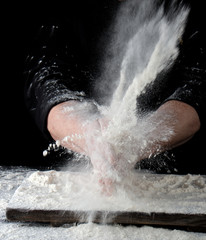 chef in black uniform sprinkles white wheat flour in different directions