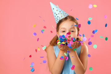 Cheerful little girl celebrates birthday. The child blows confetti from the hands. Closeup portrait...