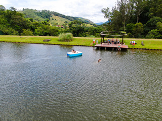 Fototapeta na wymiar Aerial view of beautiful little wood cabana next the lake in tropical mountain, with family enjoying relax sun moment, swimming and fishing. Monte Alegre Do Sul, Brazil. 