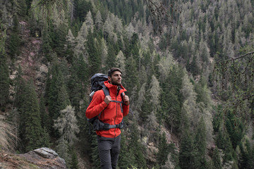 Young athletic man looking at the landscape on a backpacking adventure in the mountains. Fir forest background. Freedom, nature, wanderlust and adventure concepts.