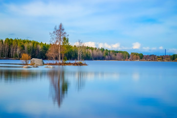 Obraz premium long exposure photography of clean water lake surrounded by pine birch trees and incredible beauty under the cloud cover blue sky