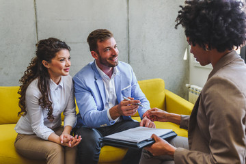 Young married couple signing real estate purchase contract  after consulting with professional broker