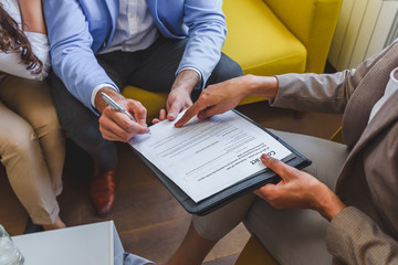 Young married couple signing real estate purchase contract  after consulting with professional...