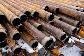 Salvaged pipes and casings are lined up on racks in storage on a California oil lease. Drill pipes with oil drops.