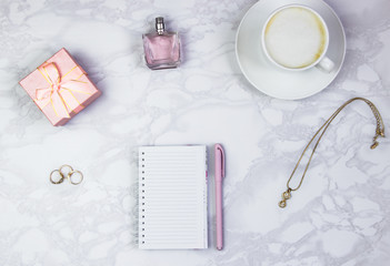 Women's accessories on a white marble table. Notepad, pen and glass of coffee on the table and other female cosmetic accessories. Beauty and fashion concept. Top view, flat lay, copy space