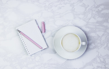 Women's accessories on a white marble table. Notepad, pen and glass of coffee on the table and other female cosmetic accessories. Beauty and fashion concept. Top view, flat lay, copy space