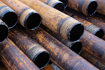 Salvaged pipes and casings are lined up on racks in storage on a California oil lease. Drill pipes with oil drops.
