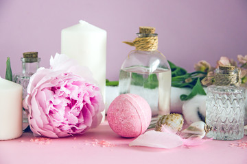 Fototapeta na wymiar Transparent glass bottles with cosmetic, bath bombs, shells, candles, fresh pink flowers, white towel, cotton boxes on a pink background. The concept of natural cosmetics and spa skin care. Copy space