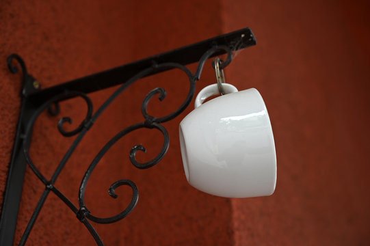 A white coffee cup that is fixed with a ring on a black metal holder.