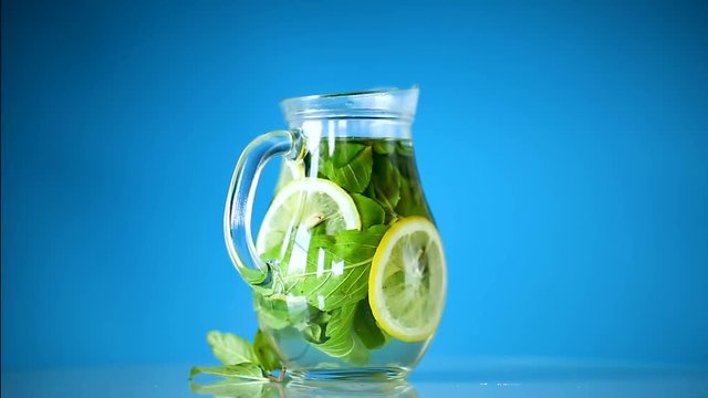 Fresh cold lemonade with lemons and mint in a carafe isolated on blue
