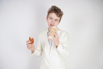 young student guy in a business suit stands with a Cup of coffee and cookies in his hands on a white background in the Studio