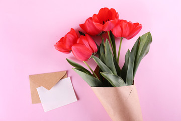 Fresh flower composition, bouquet of red color tulips, paper textured background with envelope. International Women's day, mother's day greeting concept. Copy space, close up, top view, flat lay.