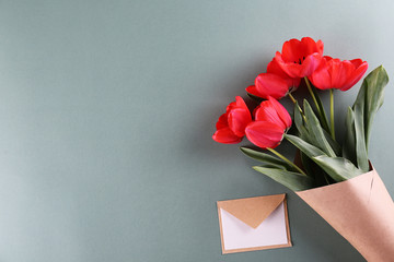 Fresh flower composition, bouquet of red color tulips, paper textured background with envelope. International Women's day, mother's day greeting concept. Copy space, close up, top view, flat lay.