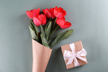 Fresh flower composition, bouquet of red color tulips, paper textured background with present. International Women's day, mother's day greeting concept. Copy space, close up, top view, flat lay.