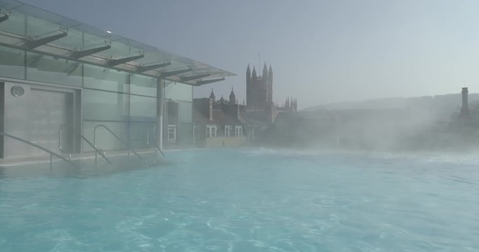 Stablised tracking shot from changing area to rootop thermal pool in historic Roman city of Bath Spa in England with Bath Abbey cityscape in the background
