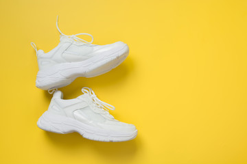 Pair of white female sneakers on yellow. Flat lay, top view minimal background.