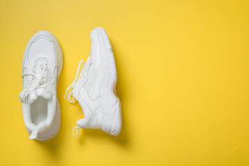 Pair of white female sneakers on yellow. Flat lay, top view minimal background.