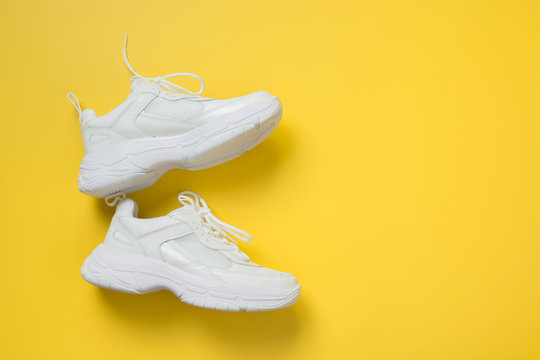 Pair of white female sneakers on yellow. Flat lay, top view minimal background.