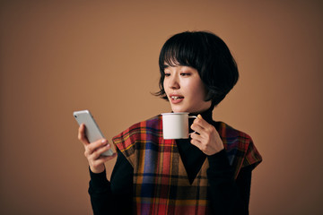 コーヒーを飲みながらスマホを操作する若い女性