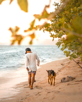 man in white long-sleeved shirt beside black dog walking on seashore