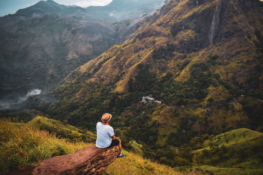 man sitting on edge of brown rock